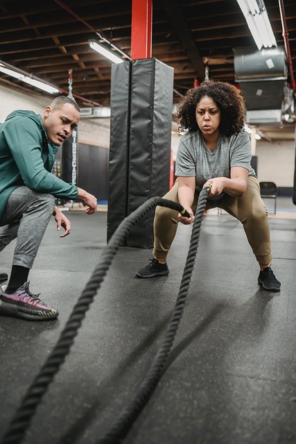 Personal trainer assists client with battle rope exercise
