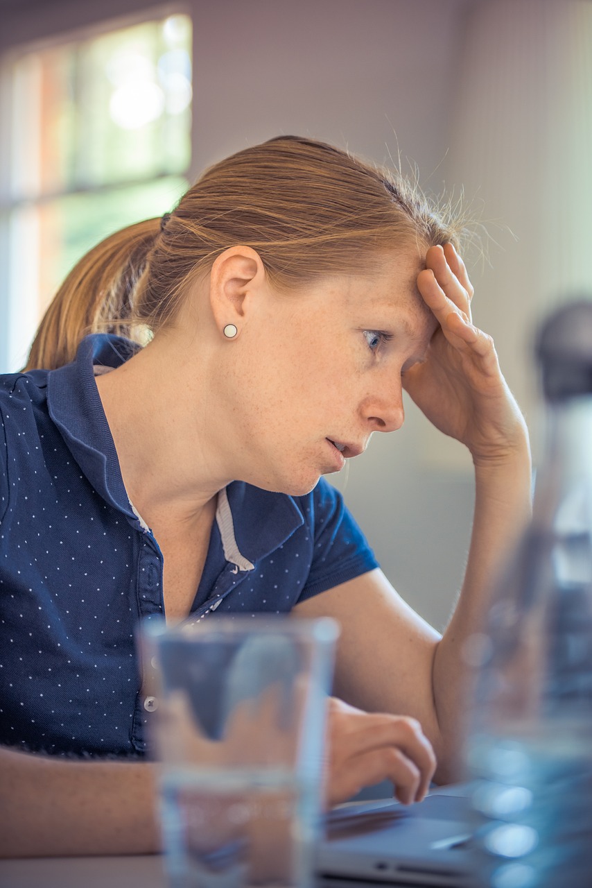 A healthcare worker holds her head, visibly stressed and overwhelmed.