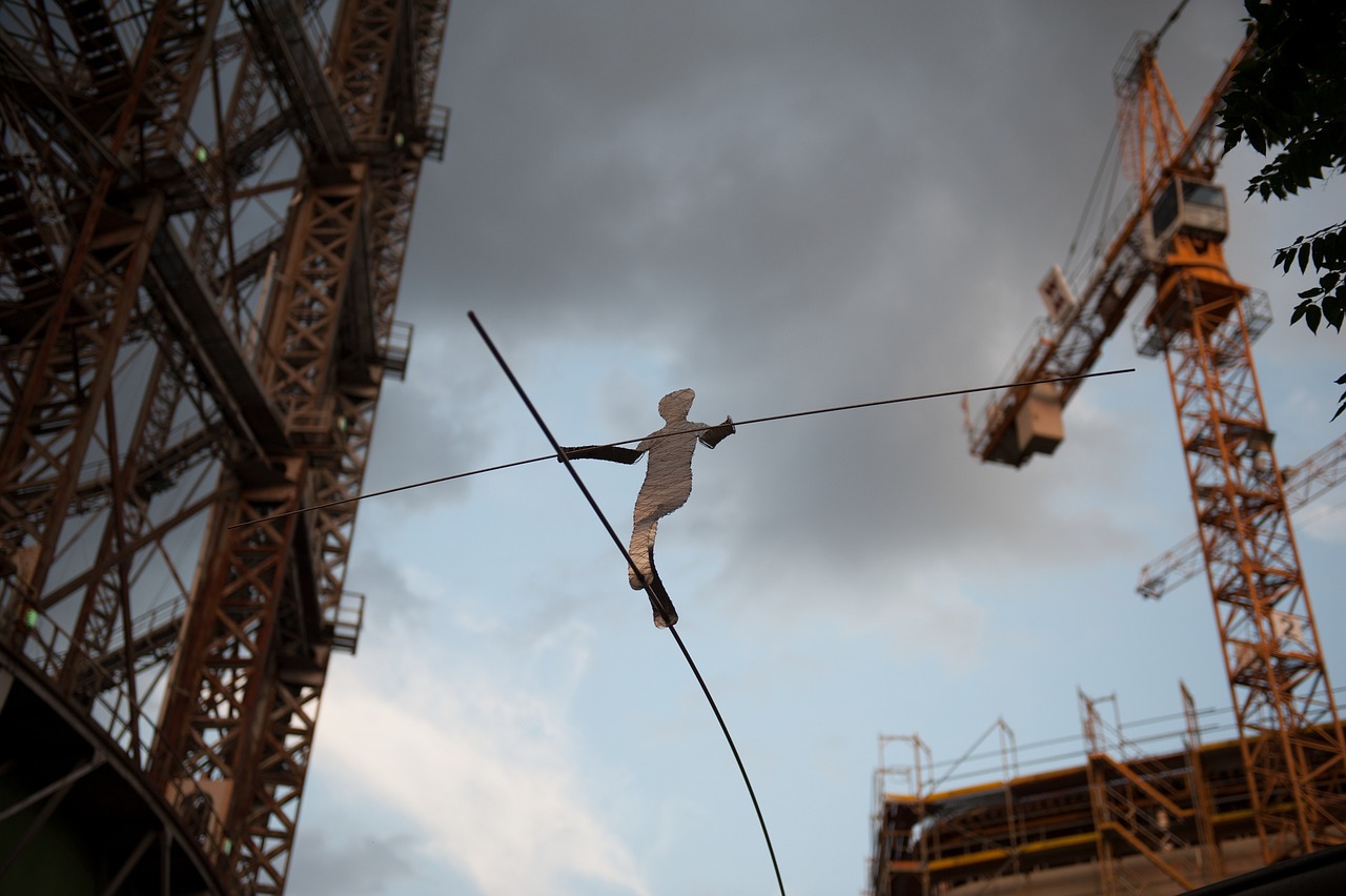 Man balances on tightrope against backdrop of construction site.