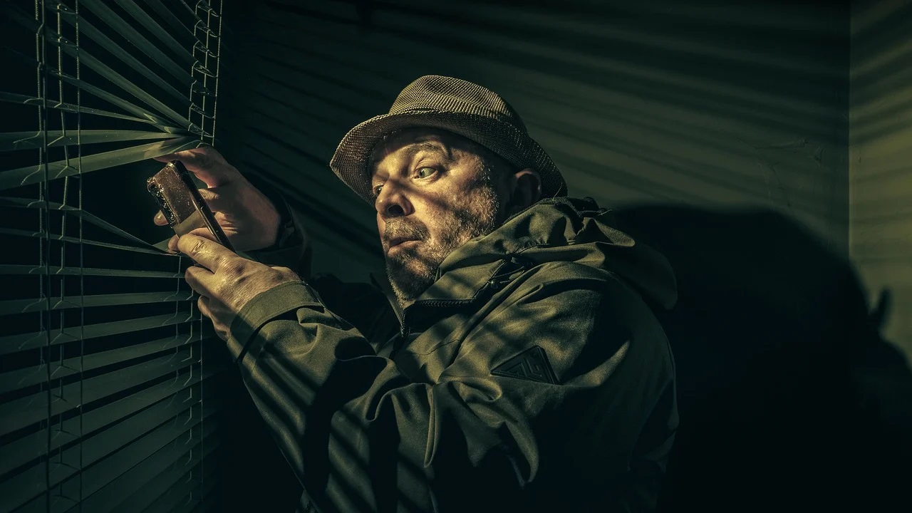Private investigator spying through the slats of a window blind.