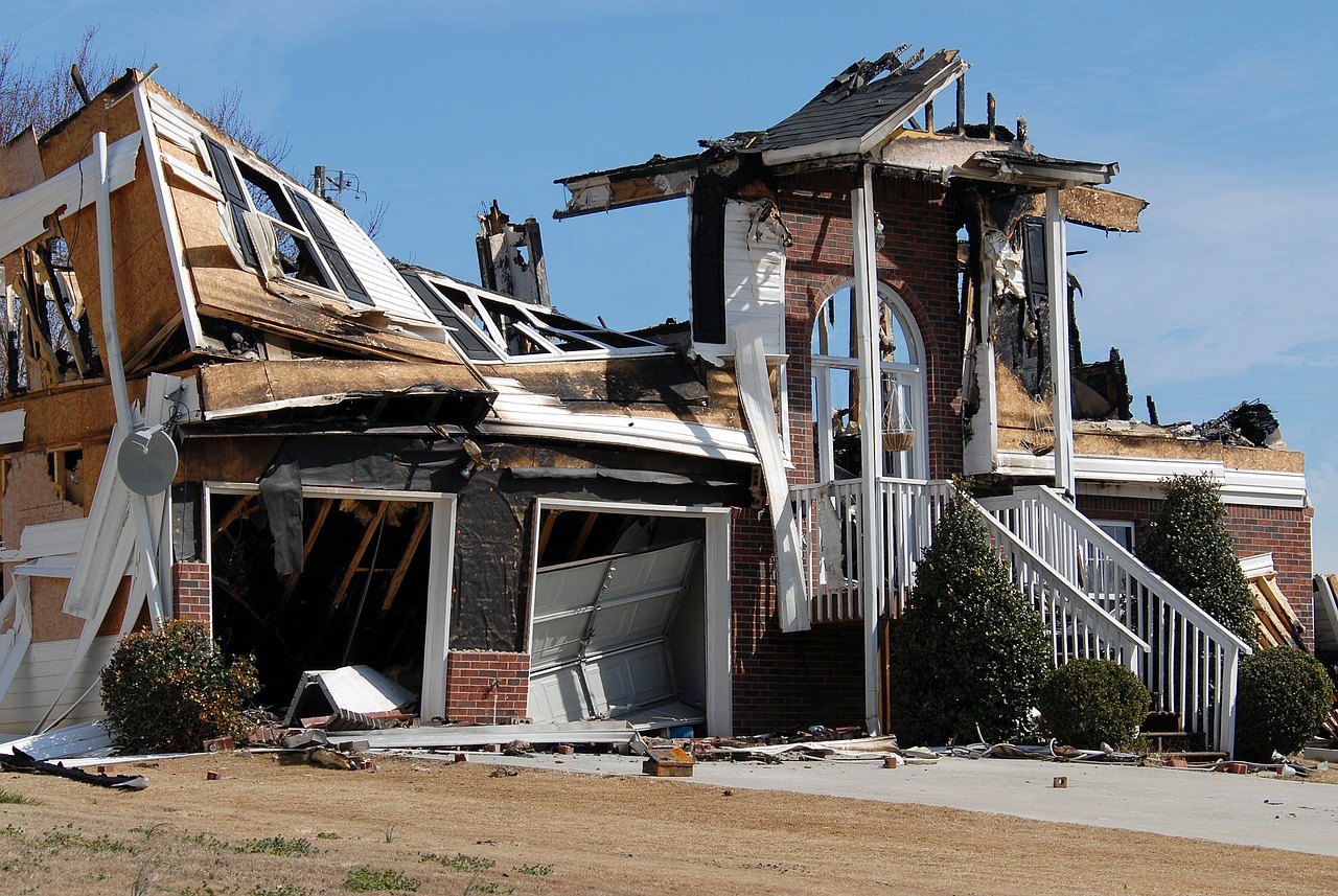 A storm-battered house stands with damaged walls; debris scattered around