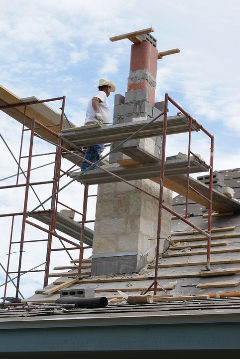 A workman repairs a water damaged chimney on a sloping roof.