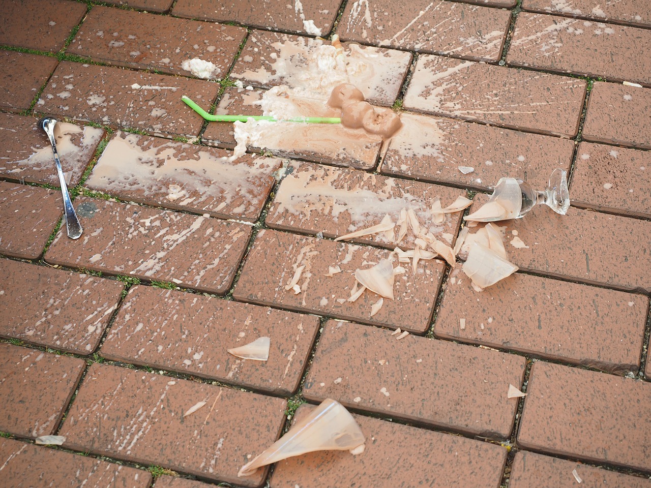 Accidental spill: Broken glass and spilled smoothie on pavement.