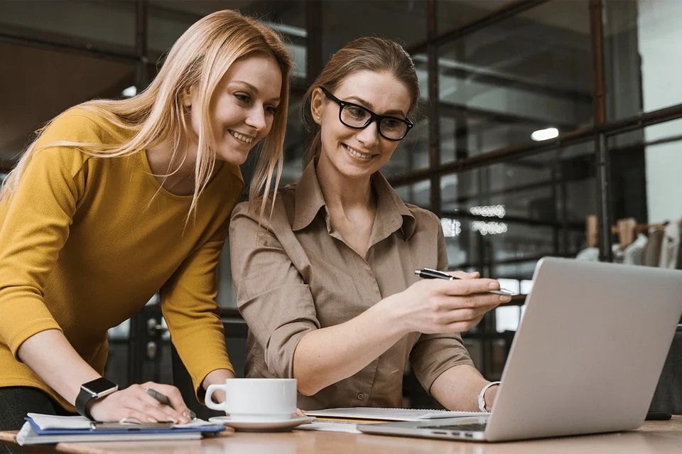 Two smiling female colleagues work together on a laptop, enjoying a productive moment.