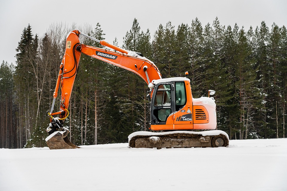 Excavator stands idle in snow-covered yard due to delayed landscaping project.