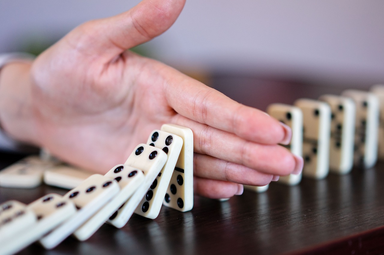 Outstretched hand halts tumbling dominoes.