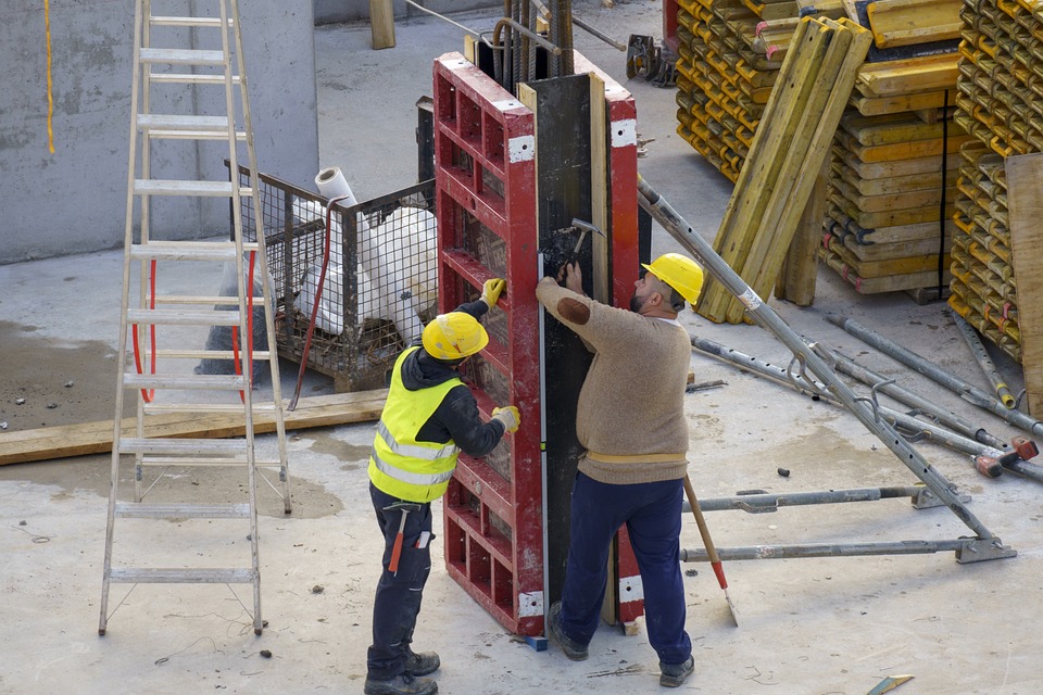 Two construction workers in hard hats board up a pillar form before concrete pour.