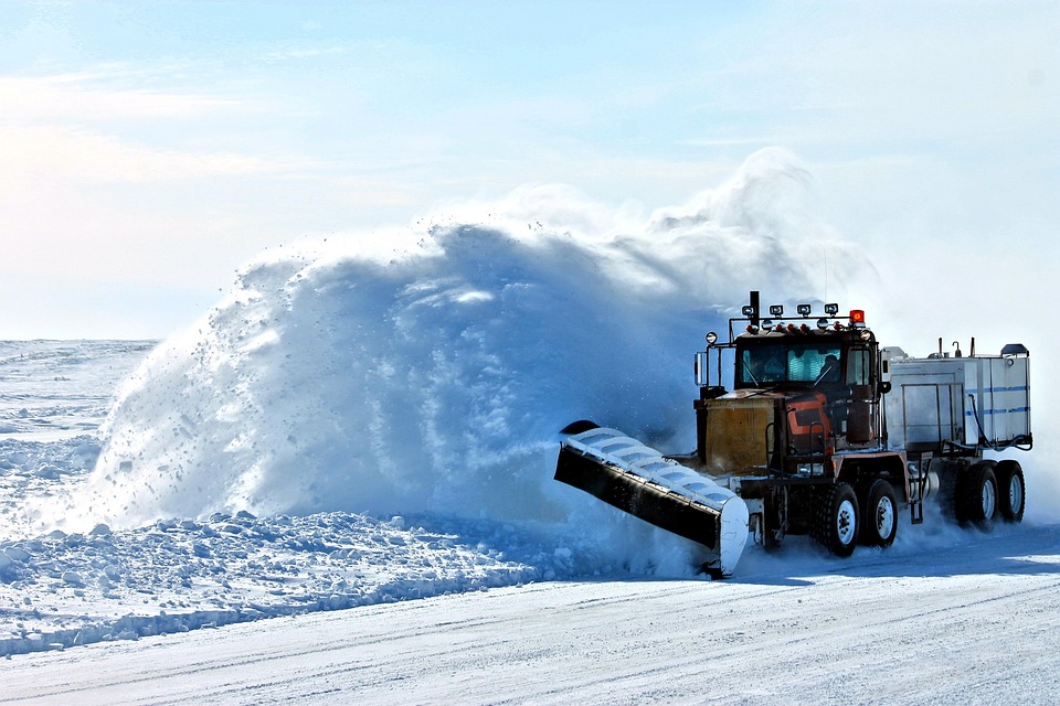 Snowplow clears snowy road, tossing plumes of snow to the side.