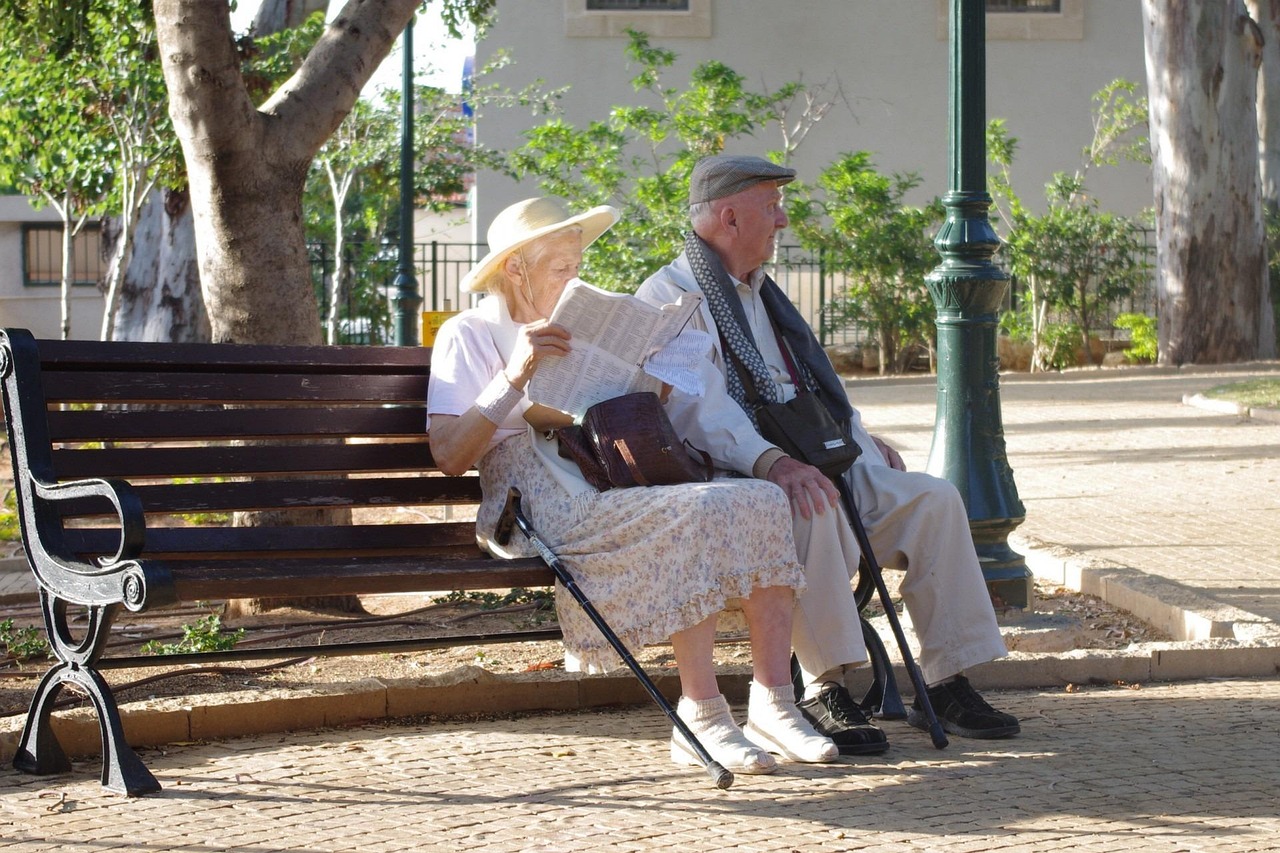 Elderly couple sit on a bench at an aged care facility.