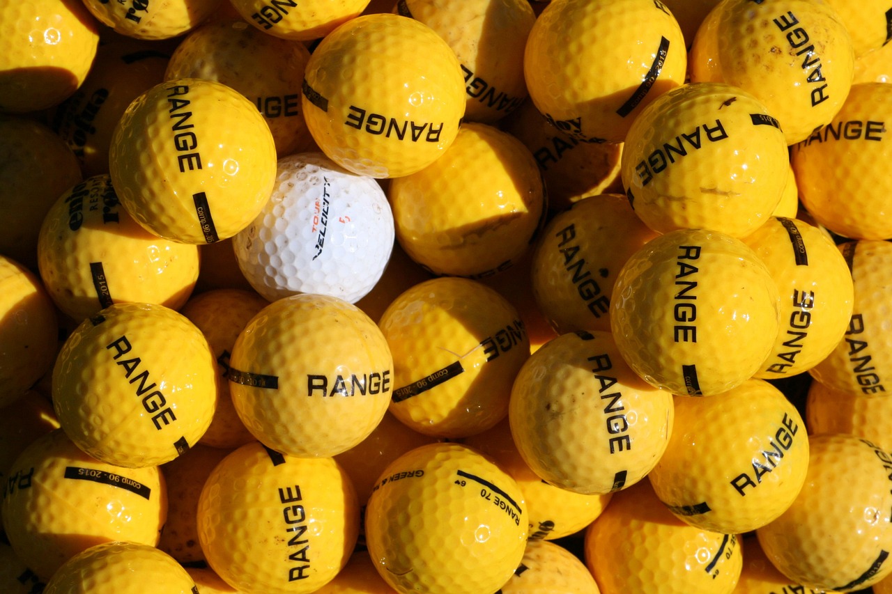 A cluster of yellow golf balls surrounds a solitary white golf ball.