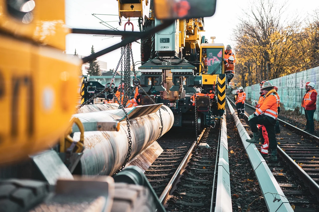 Workers in orange vests construct and repair rail tracks with heavy machinery and tools